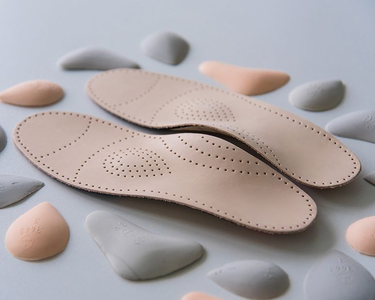 Beige Einlegesohlen mit perforierter Oberfläche, umgeben von kleinen grauen und pfirsichfarbenen Formteilen